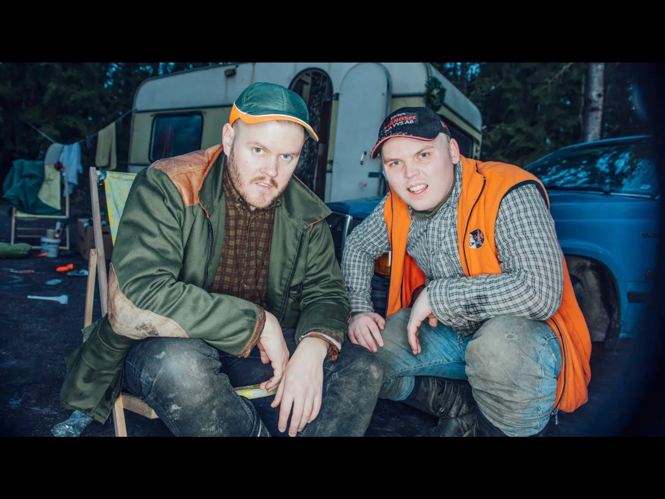 Two fat men sitting in front of husvagn
